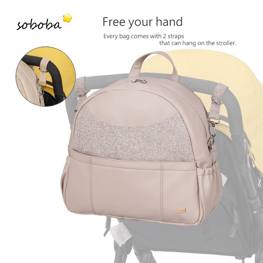 Beige vegan leather diaper bag backpack hanging on stroller with adjustable straps